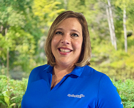 Danae Durling, Program Director at SpringHill, smiling outdoors in a blue camp polo shirt