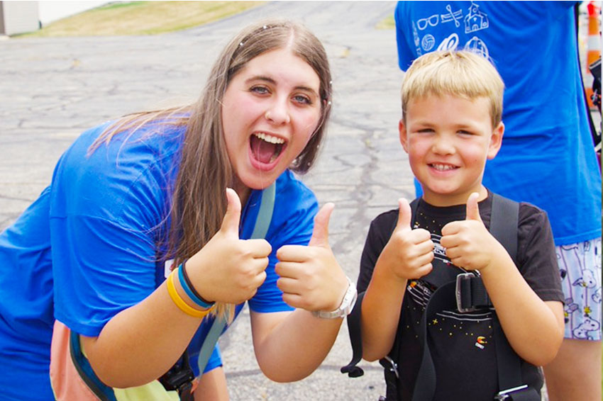 Smiling SpringHill camper and staff member giving thumbs up during outdoor activity time on campus.