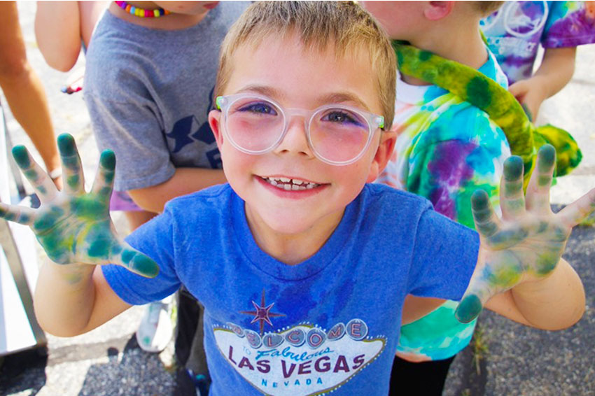 Boy smiling with paint-covered hands during outdoor craft time at SpringHill camp.